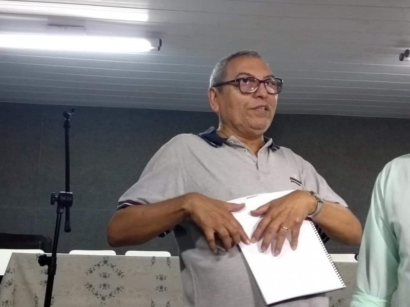 Antônio Muniz em uma foto da cintura para cima; fazendo uma leitura em Braille 